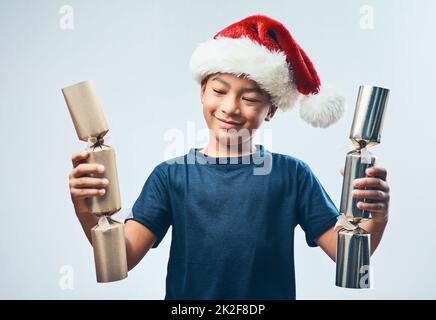 Die Feuerwehrauplosion steht bevor Studioaufnahme eines süßen kleinen Jungen mit Weihnachtsmannmütze und zwei Weihnachtskeksen vor grauem Hintergrund. Stockfoto