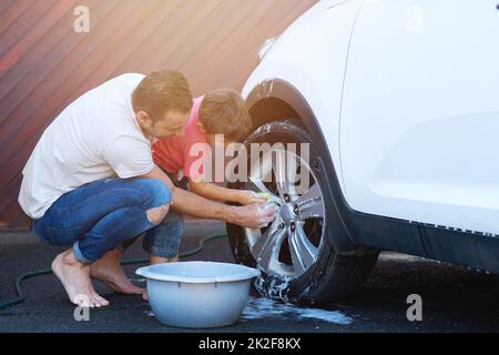 Bindung während der Waschtage. In voller Länge ein Foto von einem Vater und einem Sohn waschen das Rad eines Autos zusammen. Stockfoto