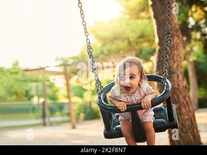 Ich liebe diesen Schwung. Aufnahme eines kleinen Mädchens, das auf einer Schaukel in einem Park spielt. Stockfoto