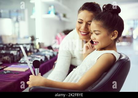 Schau, wie schön du bist. Aufnahme einer Mutter, die ihrem niedlichen kleinen Mädchen hilft, sich in einer Garderobe zu schminken. Stockfoto