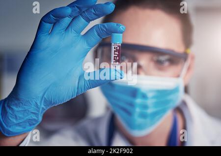 Nun, das hat lange gedauert. Nahaufnahme einer nicht erkennbaren Wissenschaftlerin, die eine schützende Gesichtsmaske trägt und ein abscheuliches Blut in einem Labor hält. Stockfoto