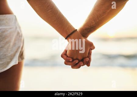 Die Wellen kommen und gehen, aber bleiben nicht ewig. Kurzer Schuss eines jungen Paares, das die Hände am Strand hält. Stockfoto