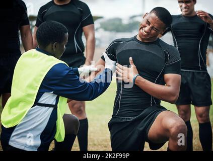 Das tut so weh. Kurzer Schuss eines jungen Rugby-Spielers, der auf dem Spielfeld erste Hilfe erhält. Stockfoto