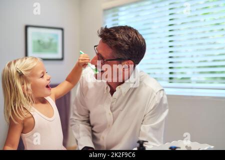 So soll man putzen, Papa. Aufnahme eines kleinen Mädchens, das ihrem Vater zu Hause beim Zähneputzen hilft. Stockfoto