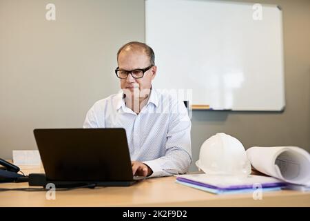 Einige Bürozeiten nach einem Tag auf der Website. Aufnahme eines fokussierten professionellen Geschäftsmannes, der an seinem Laptop arbeitet, während er in einem Büro sitzt. Stockfoto