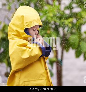 Bleibt diesen Winter wasserdicht. Ein entzückender kleiner Junge spielt draußen im Regen. Stockfoto