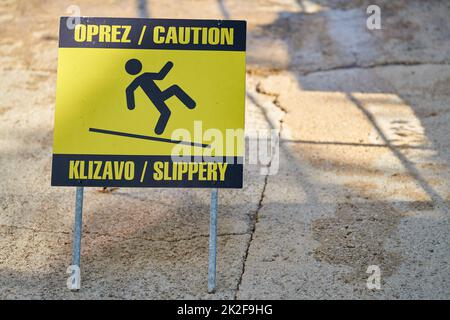 Schild mit der Aufschrift Achtung rutschig in kroatischer und englischer Sprache in der Altstadt von Krk in Kroatien Stockfoto