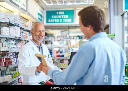 Er weiß, was seine Kunden brauchen. Kurzer Schuss eines hübschen reifen männlichen Apothekers, der einem Kunden in der Apotheke hilft. Stockfoto