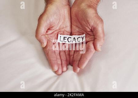 Was ist deine Geschichte? Ausgeschnittene Aufnahme einer Person, die ein Stück Papier mit dem Wort Vermächtnis darauf hält. Stockfoto