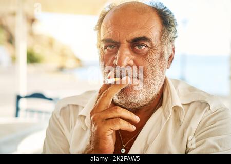 Er ist ein harter Kerl. Porträt eines selbstbewussten älteren Mannes, der eine Zigarette raucht und draußen steht, während er auf die Kamera schaut. Stockfoto