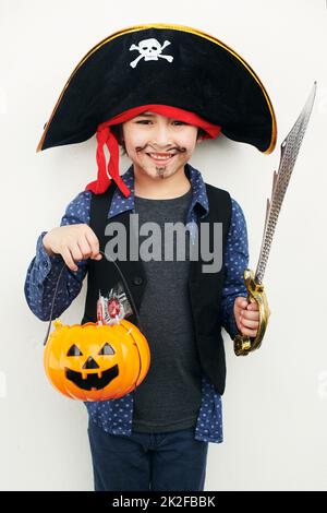 Verspielter Pirat. Aufnahme eines kleinen Jungen, der in einem Piratenkostüm gekleidet ist, während er einen Buben oder eine Laterne vor einem weißen Hintergrund hält. Stockfoto