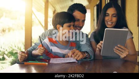 Mütter färben online ein, während wir auf Papier färben. Zugeschnittene Aufnahme einer jungen Familie, die sich in einem Tablet am Tisch im Freien einfärbt. Stockfoto