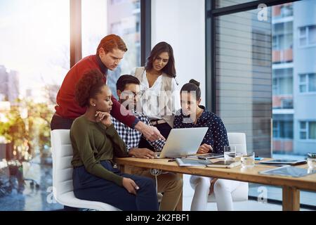 Spielen mit ein paar Ideen. Aufnahme einer Gruppe von Designern, die im Sitzungssaal etwas auf einem Laptop diskutieren. Stockfoto