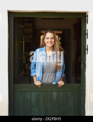 Keine Sorge, sei glücklich. Porträt einer attraktiven jungen Frau, die an ihrer Hintertür steht. Stockfoto