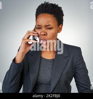 Hört mir einfach zu und tut, was ich sage. Ausgeschnittene Aufnahme einer wütenden Geschäftsfrau, die auf einem Mobiltelefon vor grauem Hintergrund spricht. Stockfoto