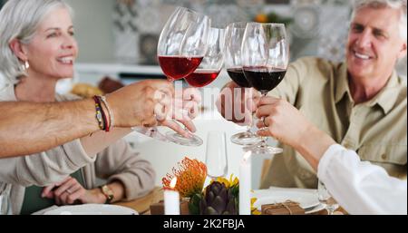 Heres an Freunde, die sich wie eine Familie fühlen. Aufnahme von zwei glücklichen Paaren, die sich zum Mittagessen hinsetzen und zu Hause mit Weingläsern toasten. Stockfoto