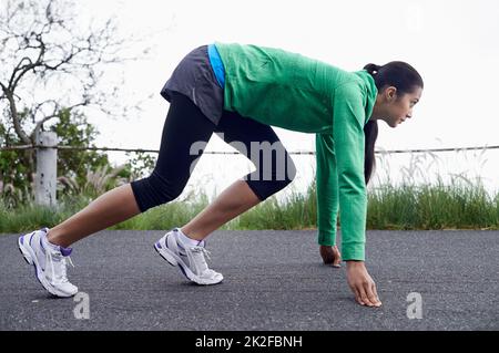 Bereit, diesen Weg zu ihrem eigenen zu machen Eine junge Frau, die auf der Straße hockend, um zu laufen. Stockfoto