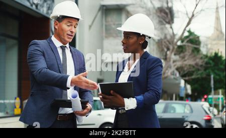 Gemeinsam die Stadt zum Besseren entwickeln. Aufnahme von zwei Geschäftsleuten in Harthüten, die draußen in der Stadt eine Diskussion führen. Stockfoto