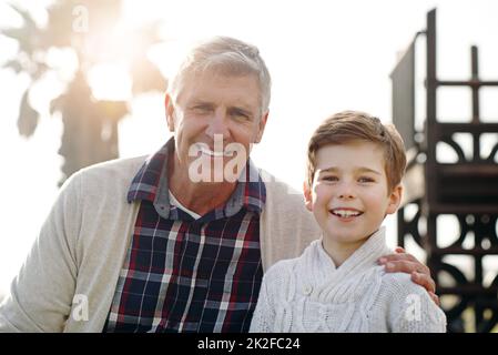 Es ist sicher zu sagen, dass Ive die guten Gene weitergegeben hat. Porträt eines entzückenden kleinen Jungen, der mit seinem Großvater posiert, während er sich im Freien entspannt. Stockfoto