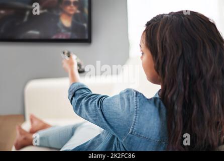 Vor dem fernseher. Aufnahme einer jungen Frau, die zu Hause Fernsehen schaut. Stockfoto