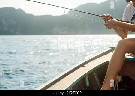 Seine Linie werfen. Kurzer Schuss eines nicht erkennbaren jungen Mannes, der auf seinem Boot auf See fischt. Stockfoto