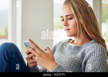 Schicken Sie einige Texte an ihre Freunde. Ausgeschnittene Aufnahme einer attraktiven jungen Frau, die eine SMS sendet, während sie sich zu Hause abkühlt. Stockfoto