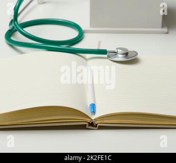 Offenes leeres Notizbuch mit Stift und Stethoskop, weißer Tisch Stockfoto