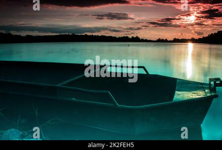 Die untergehende Sonne über dem See mit einem Boot Stockfoto