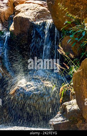 Kleiner Wasserfall, der zwischen Steinen scheint Stockfoto