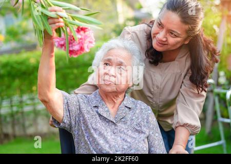 Asiatische ältere Frau genießen im Blumengarten mit Betreuer im Park. Stockfoto