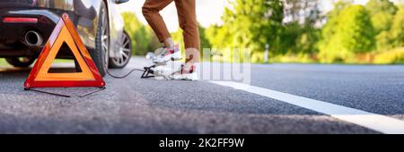 Frau pumpt das Rad des Autos am Straßenrand hoch Stockfoto