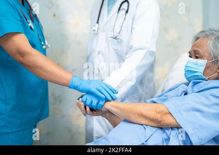 Das asiatische Ärzteteam und die alte ältere Patientin legen sich die Hände als Team zusammen, um neue Normalität zur Behandlung des Covid-19 Coronavirus auf der Krankenhausstation zu motivieren. Stockfoto