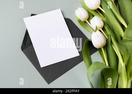 Mockup Papier leere Einladung oder Grußkarte und Strauß von weißen Tulpen. Stockfoto