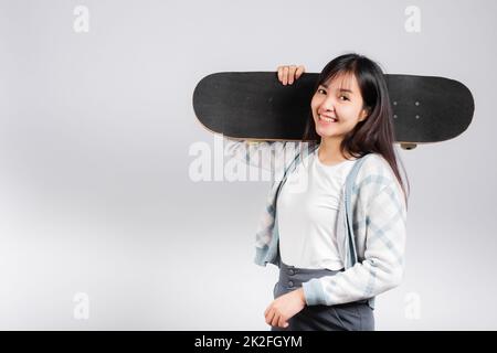 Lächelnde glückliche Frau, die Skateboard auf der Schulter hält