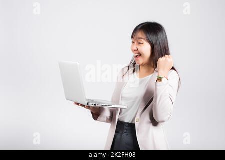 Eine Frau, die selbstbewusst mit ihrem Laptop herumlächelt und den Erfolg feiern möchte Stockfoto