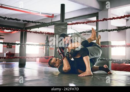 Wie soll er da rauskommen? Aufnahme von zwei jungen männlichen Boxern, die sich während eines Trainingspartnerspiels in einem Boxring auf dem Boden im Fitnessstudio gegenüberstehen. Stockfoto