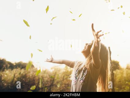 Kleines blondes Mädchen spielt mit grenblättern im Garten, lächelt, hat Spaß, lacht Stockfoto