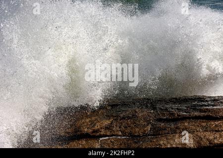 Starke Welle bricht über Felsen und Wasser spritzt in die Luft Stockfoto