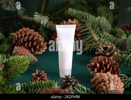 Natürliche organische Kosmetikcreme in weißer Kunststoffröhre in der Nähe von Tannenästen und Kiefernzapfen auf dunkelgrüner Nahaufnahme Stockfoto