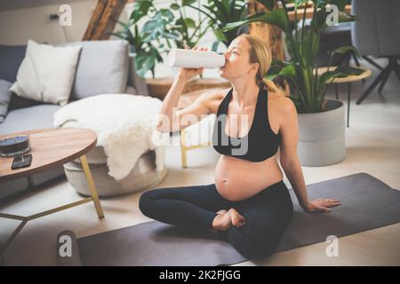 Junge glückliche und fröhliche schöne Schwangere, die eine Pause macht, feuchtigkeitsspendend, Trinkwasser aus dem Botle nach Hause Wohlbefinden Training progrem. Stockfoto