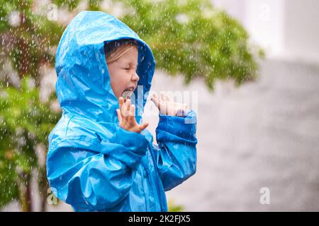 Um den Regenbogen zu genießen, genießt zuerst den Regen. Ein junges Mädchen spielt draußen im Regen. Stockfoto