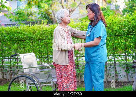 Pfleger Hilfe asiatische ältere Frau Behinderung Patient sitzt im Rollstuhl im Park, medizinisches Konzept. Stockfoto