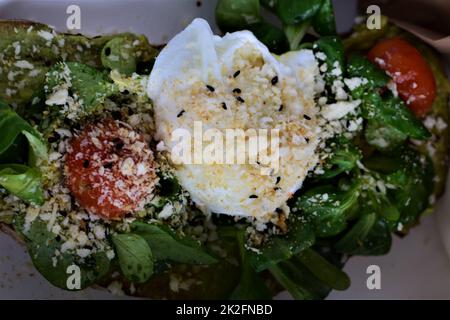 Pochiertes Ei auf Salat mit zwei Tomaten als Nahaufnahme Stockfoto