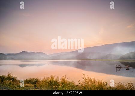 Idyllisch dramatischer Sonnenuntergang mit der Szene von Nebel über den Lake Mountains im Hintergrund am Khao Luang Reservoir. In Sukhothai Thailand Stockfoto