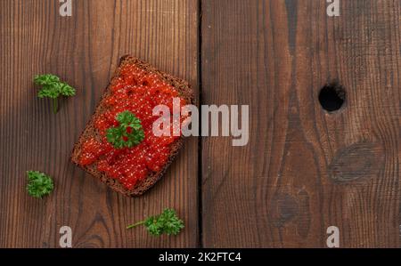 Kaviar aus rotem Lachs liegt auf einem Stück Roggenbrot. Brauner Holztisch Stockfoto