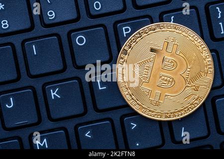 Ein goldenes Bitcoin auf dunkler Tastatur des Computers Stockfoto