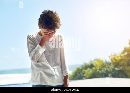 Jemand fühlt sich heute unten. Ein kurzer Schuss eines kleinen Jungen, der sein Gesicht vor Traurigkeit bedeckt. Stockfoto