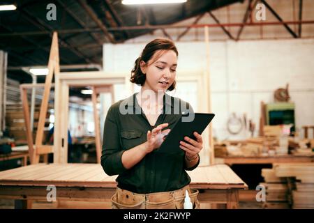 Sehen wir uns unsere Online-Bestellungen an. Aufnahme einer Tischlerin mit einem digitalen Tablet in ihrer Werkstatt. Stockfoto