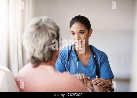 Ich bin immer für Sie da. Eine kurze Aufnahme einer attraktiven jungen Krankenschwester, die die Hände einer älteren Frau bequem in der Hand hält. Stockfoto