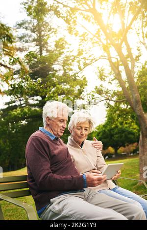 Mit den Gadgets dieser Generation Schritt halten. Aufnahme eines älteren Paares, das zusammen ein digitales Tablet im Park benutzt. Stockfoto